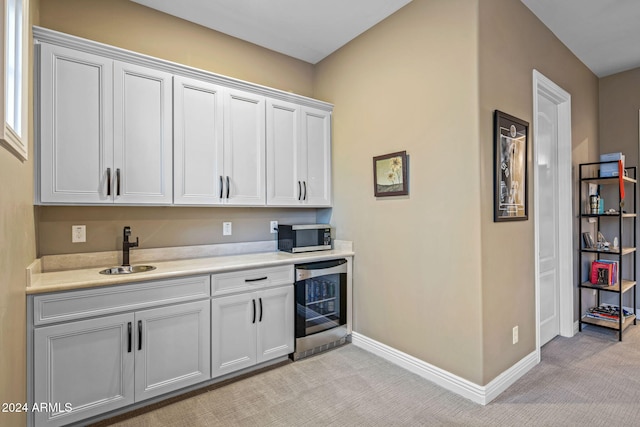 kitchen with wine cooler, light colored carpet, light countertops, stainless steel microwave, and a sink