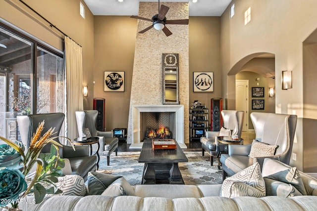 living room with arched walkways, ceiling fan, a fireplace, and a high ceiling