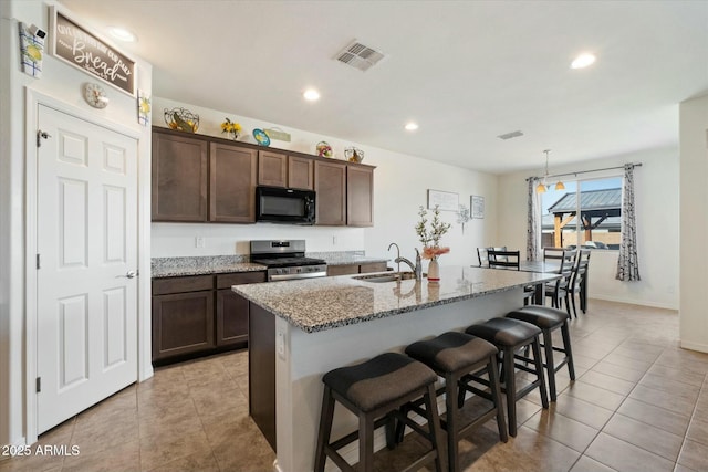 kitchen featuring sink, a center island with sink, stainless steel range, light stone countertops, and a kitchen bar