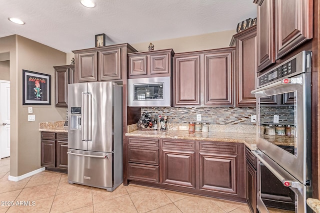 19427 W Colter St, Litchfield Park, AZ 85340 - kitchen featuring stainless steel appliances, backsplash, light tile patterned floors, light stone counters, and dark brown cabinets