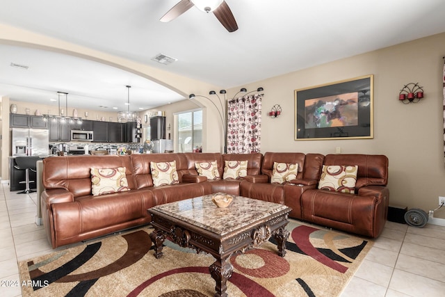 tiled living room with ceiling fan with notable chandelier