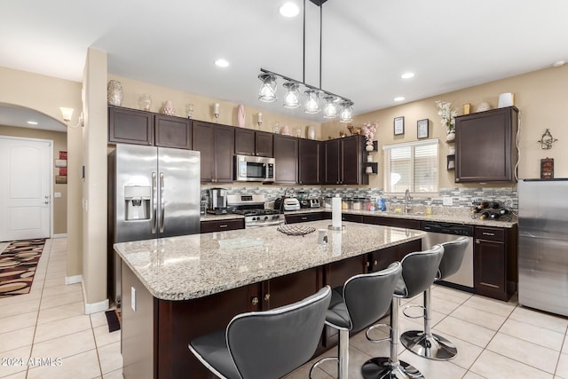 kitchen with a kitchen island, pendant lighting, dark brown cabinets, light tile patterned flooring, and appliances with stainless steel finishes