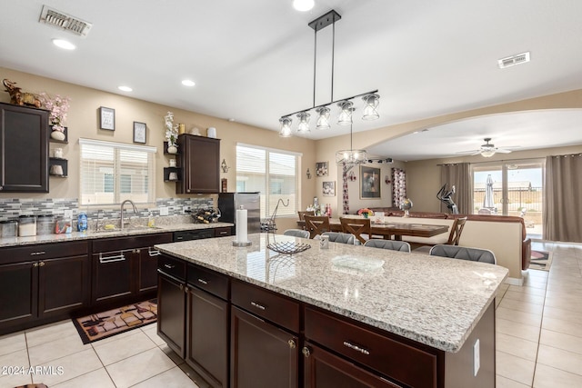 kitchen with tasteful backsplash, ceiling fan, sink, a kitchen island, and hanging light fixtures