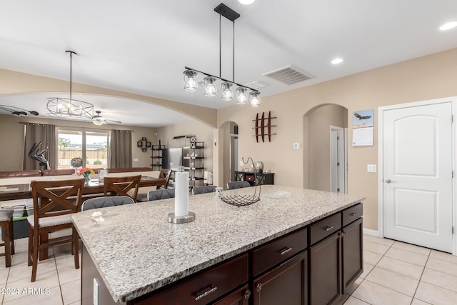 kitchen with light tile patterned flooring, ceiling fan, decorative light fixtures, a kitchen island, and dark brown cabinetry