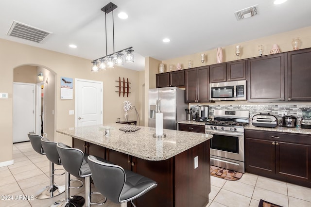 kitchen with a kitchen bar, appliances with stainless steel finishes, backsplash, pendant lighting, and a kitchen island