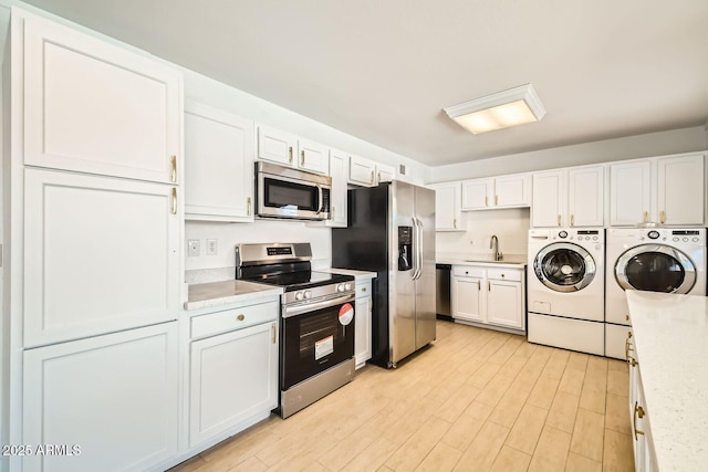 kitchen with stainless steel appliances, white cabinetry, sink, and washing machine and clothes dryer