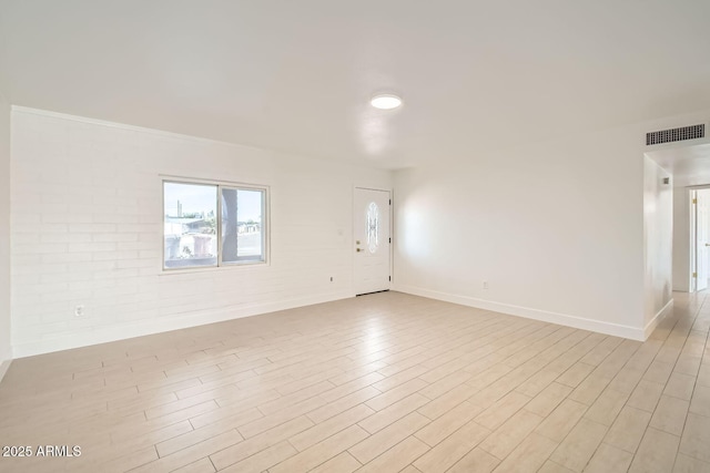 empty room featuring light wood-style floors, baseboards, brick wall, and visible vents