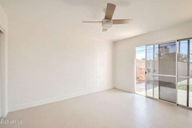 empty room with a wealth of natural light, ceiling fan, and brick wall