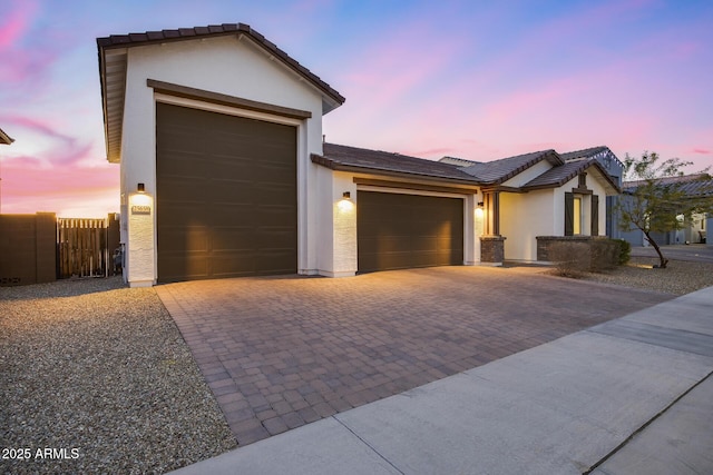 view of front of property featuring a garage, fence, decorative driveway, and stucco siding