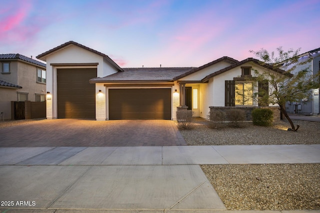 view of front facade with a garage, decorative driveway, a tiled roof, and stucco siding