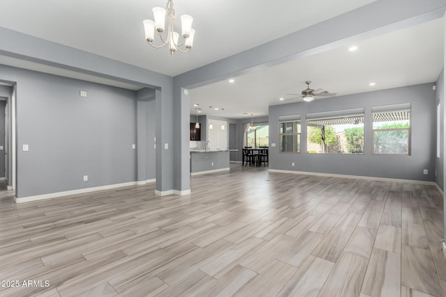 unfurnished living room with baseboards, recessed lighting, light wood-style flooring, ceiling fan with notable chandelier, and a sink