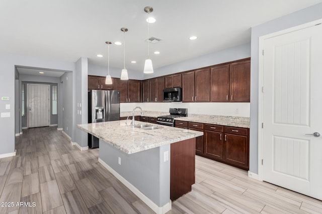 kitchen featuring a sink, dark brown cabinets, light stone countertops, stainless steel appliances, and a kitchen island with sink