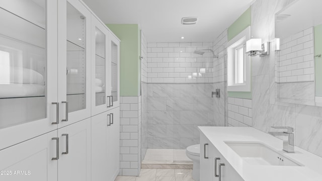 bathroom featuring tiled shower, toilet, and tile walls