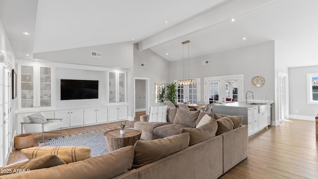 living area with visible vents, beam ceiling, light wood-style flooring, an inviting chandelier, and baseboards