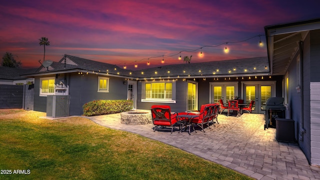 back of house at dusk featuring french doors, a patio, a fire pit, and a yard