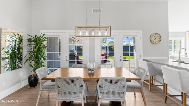 dining space featuring wood finished floors, visible vents, baseboards, french doors, and a towering ceiling