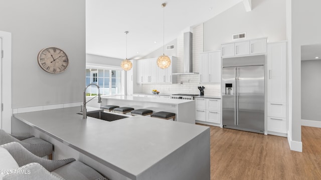 kitchen with visible vents, built in refrigerator, a kitchen breakfast bar, wall chimney exhaust hood, and a sink