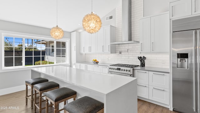 kitchen featuring decorative backsplash, wall chimney exhaust hood, high end appliances, and wood finished floors