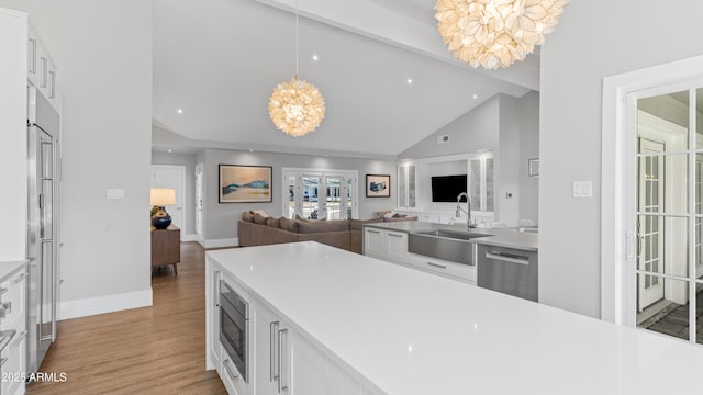 kitchen with a sink, stainless steel appliances, light wood-style floors, white cabinetry, and a notable chandelier