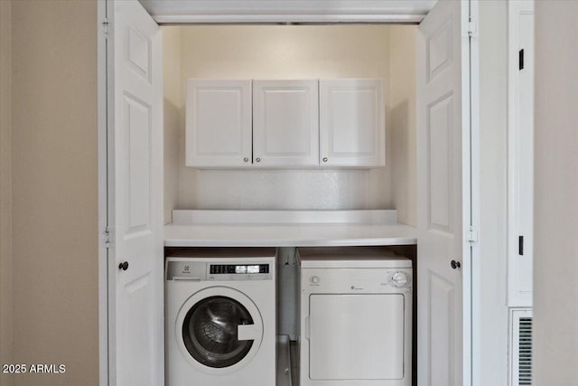 clothes washing area featuring washing machine and dryer and cabinet space