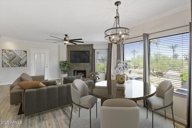 dining space featuring baseboards, a large fireplace, ceiling fan with notable chandelier, and crown molding