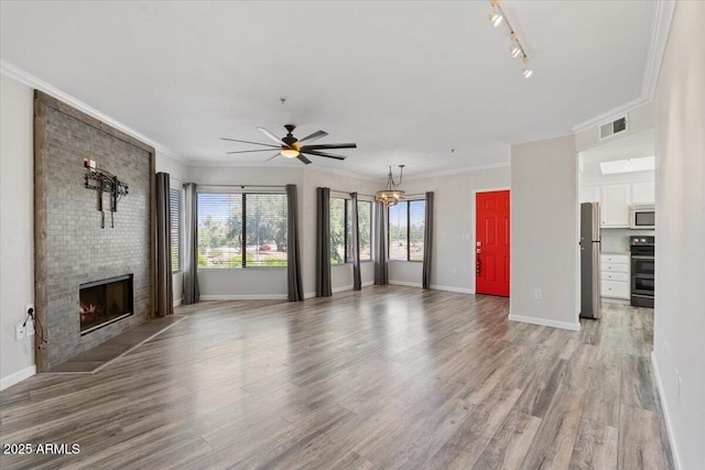 unfurnished living room with a brick fireplace, visible vents, light wood-style flooring, and ceiling fan with notable chandelier