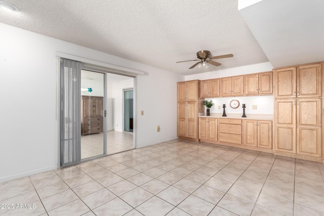 interior space featuring ceiling fan, light tile patterned flooring, a textured ceiling, and light brown cabinetry