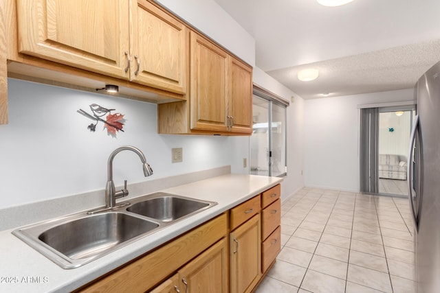 kitchen with light brown cabinetry, sink, a textured ceiling, light tile patterned floors, and stainless steel fridge