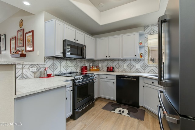 kitchen featuring tasteful backsplash, light stone countertops, light wood-type flooring, and black appliances