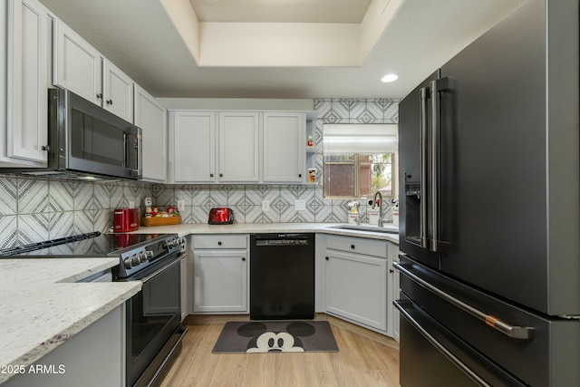 kitchen with black appliances, sink, white cabinets, a tray ceiling, and light stone countertops