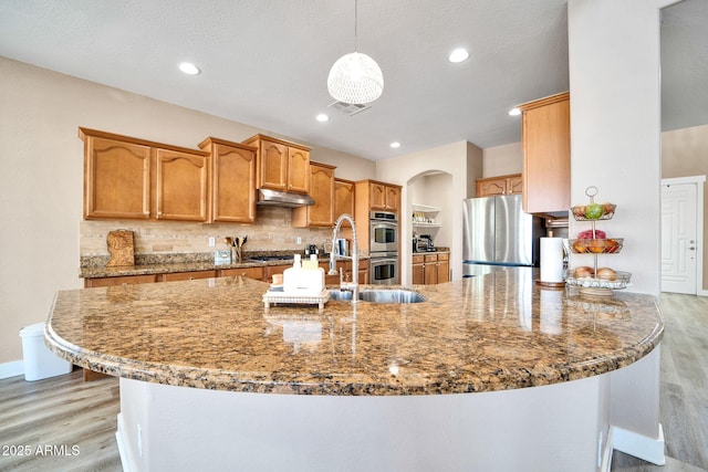 kitchen featuring stainless steel appliances, dark stone countertops, kitchen peninsula, light hardwood / wood-style floors, and decorative light fixtures