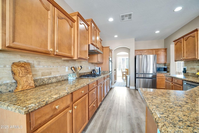 kitchen with decorative backsplash, light stone countertops, stainless steel appliances, and light hardwood / wood-style flooring