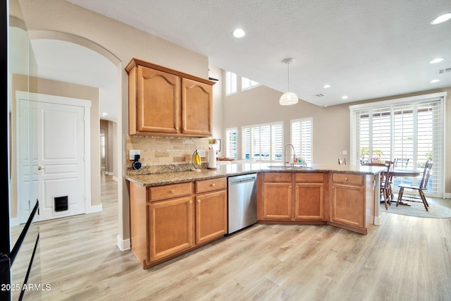 kitchen with kitchen peninsula, stainless steel dishwasher, sink, light hardwood / wood-style floors, and hanging light fixtures