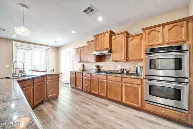 kitchen featuring light stone countertops, sink, stainless steel appliances, light hardwood / wood-style flooring, and pendant lighting