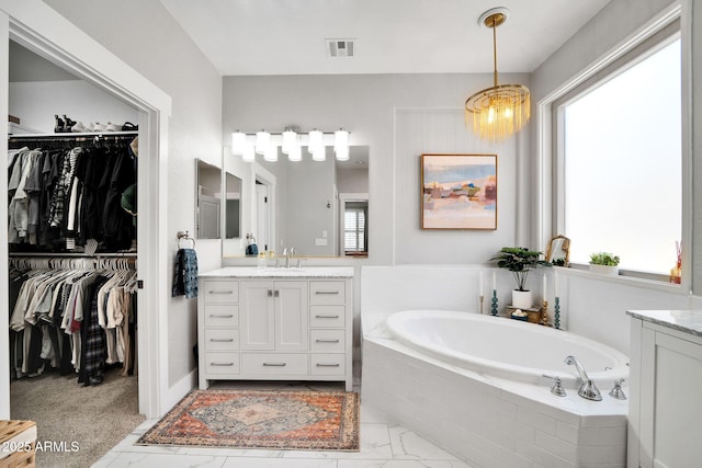 bathroom with a chandelier, vanity, and tiled tub