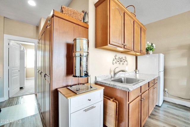 kitchen with white cabinetry, sink, white refrigerator, and light hardwood / wood-style flooring