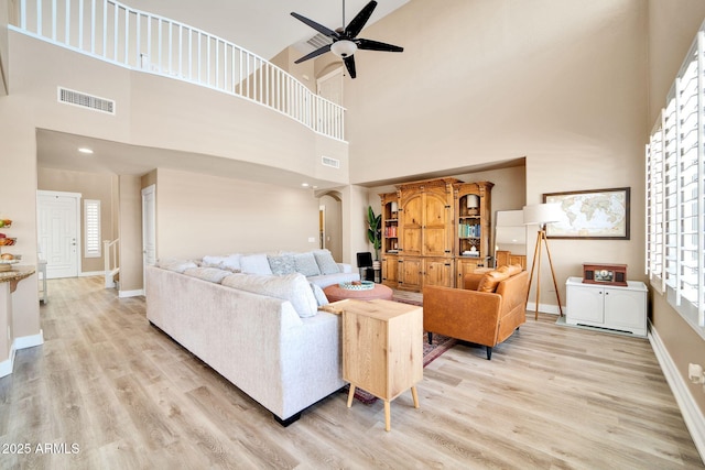 living room with light wood-type flooring, a towering ceiling, plenty of natural light, and ceiling fan