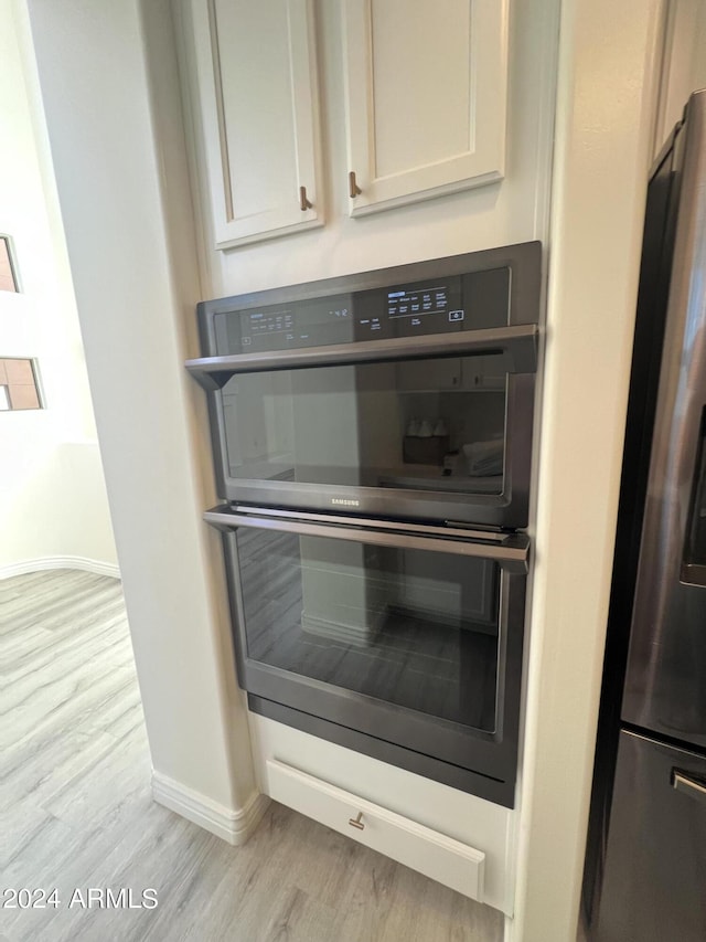 details featuring stainless steel refrigerator, black double oven, and light hardwood / wood-style flooring