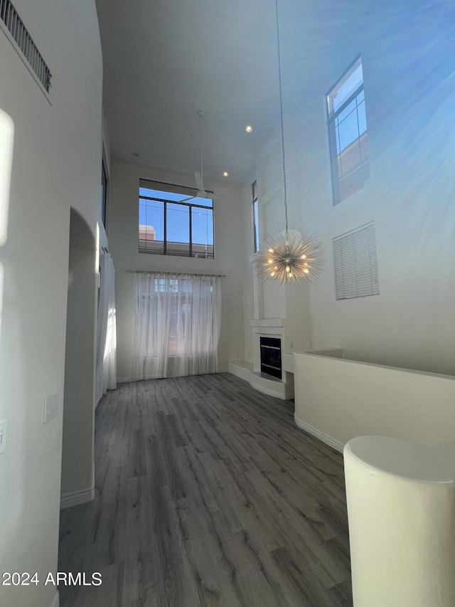 unfurnished living room featuring a towering ceiling, dark hardwood / wood-style floors, and a chandelier