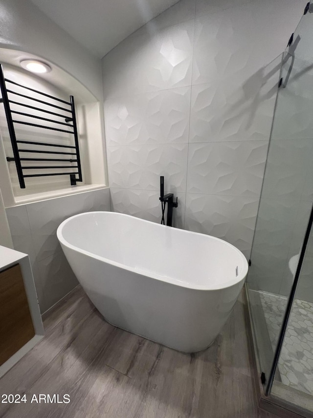 bathroom with wood-type flooring, a tub, radiator heating unit, and tile walls