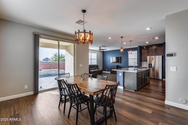 dining space featuring ceiling fan with notable chandelier, dark wood-type flooring, and sink