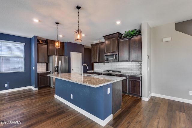 kitchen with a center island with sink, backsplash, light stone counters, and sink