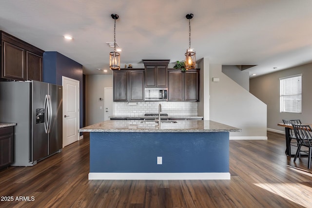 kitchen featuring appliances with stainless steel finishes, tasteful backsplash, light stone counters, dark brown cabinetry, and pendant lighting