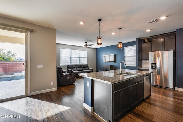 kitchen featuring sink, light stone counters, backsplash, a kitchen island with sink, and appliances with stainless steel finishes