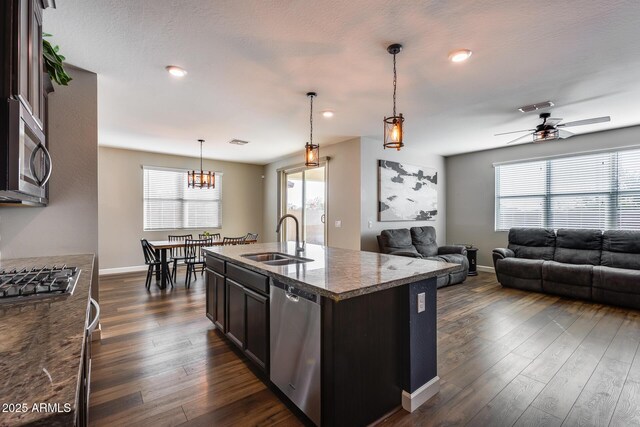 kitchen with sink, stainless steel appliances, dark hardwood / wood-style flooring, stone countertops, and a kitchen island with sink