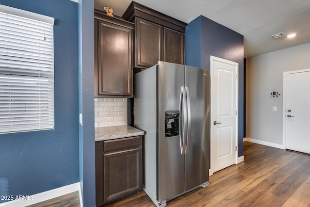 kitchen featuring dark wood-type flooring, stainless steel fridge with ice dispenser, tasteful backsplash, light stone counters, and dark brown cabinetry