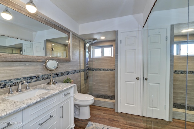 bathroom featuring tile walls, toilet, decorative backsplash, a stall shower, and wood finished floors
