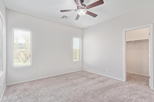 unfurnished bedroom featuring ceiling fan, a walk in closet, light colored carpet, and multiple windows