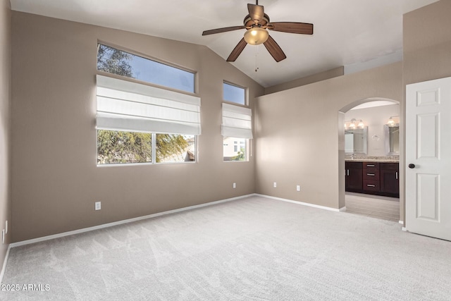 unfurnished bedroom with ensuite bath, ceiling fan, vaulted ceiling, and light carpet