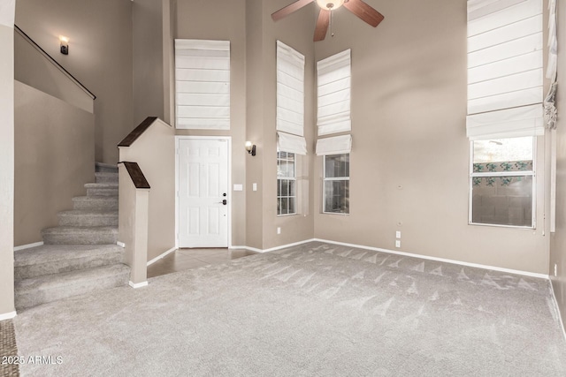 foyer with a towering ceiling, light carpet, and ceiling fan